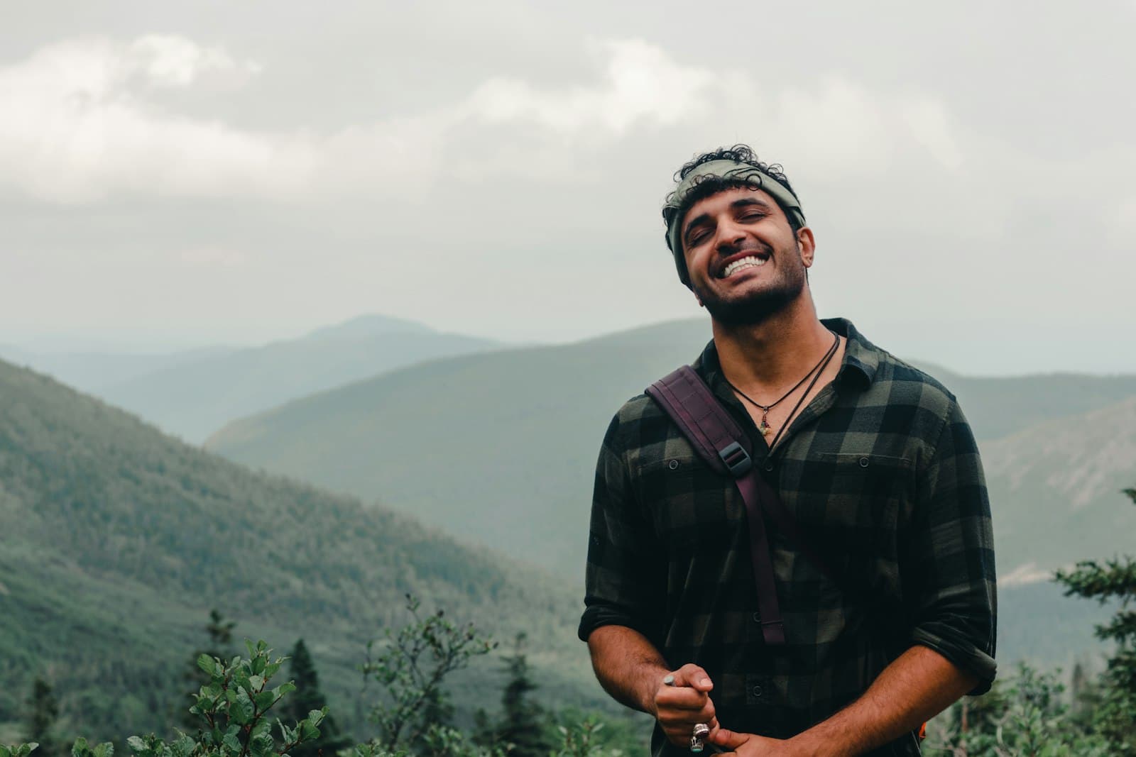A smiling guide with a shoulder bag on a hillside, mountains behind him